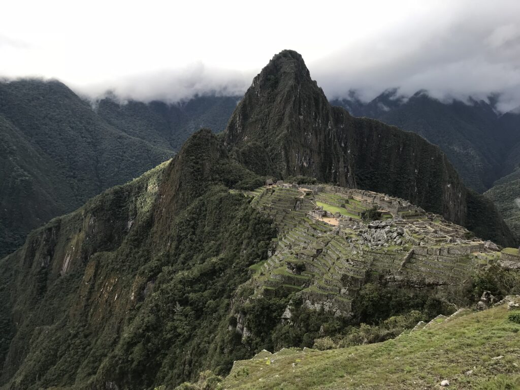 Misty mountains with ancient ruins and lush greenery under cloudy sky.